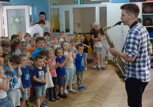 Dzieci stoją i słuchają "Lato z radiem" granego na saksofonie.