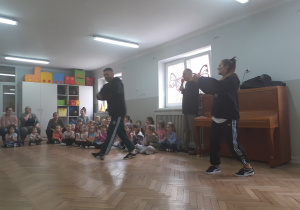 Dzieci spiedzą i oglądają pokaz tańca breakdance