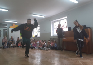 Dzieci spiedzą i oglądają pokaz tańca breakdance