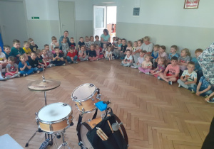 Dzieci słuchają o instrumentach perkusyjnych siedząc na podłodze.