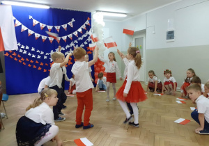 Dzieci wykonują układ taneczny z biało czerwonymi flagami w rękach
