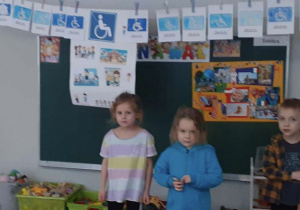 dzieci pozują na tle wykonanych prac plastycznych i plakatu dotyczącego osób niepełnosprawnych