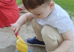 Chłopiec siedzi w piaskownicy i wsypuje piasek do wiaderka