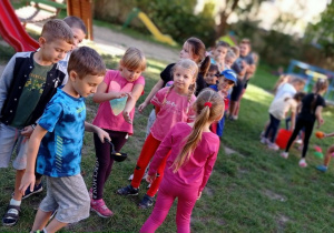 Chłopiec przenosi piłkę na łyżce, dzieci stoją i się przyglądają