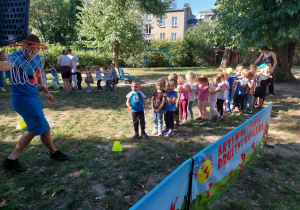 Dzieci stoją i kolejno rzucają piłkę do kosza