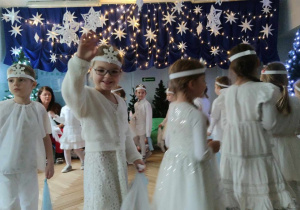 Dzieci w białych strojach tańczą taniec śnieżynek.