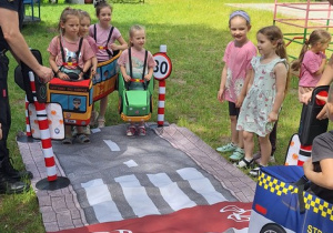 Ćwiczenia praktyczne bezpiecznego przechodzenia przez ulicę pod okiem "strażników" na macie. Jedna grupa dzieci jest przechodniami i przechodzi po pasech, a druga autami wcieliła się w rolę kierowców