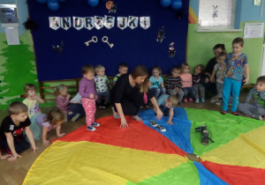 Dzieci na kolorowej chuście ustawiają swoje buty wg wyrzuconych oczek na kostce
