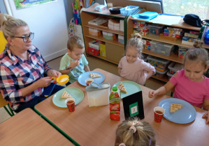 Dzieci siedzą przy stoliku i jedzą gofry z cukrem pudrem