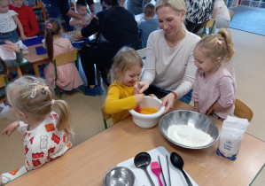 Dziewczynka miesza ciasto na gofry, mama trzyma miskę z ciastem