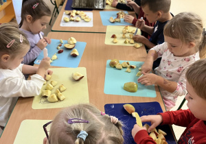 Dzieci siedzą przy stoliczkach i kroją jabłka na cząstki