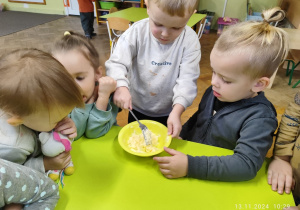 Dzieci siedzą przy stoliczku, mieszają w miseczkach czosnek z masełkiem