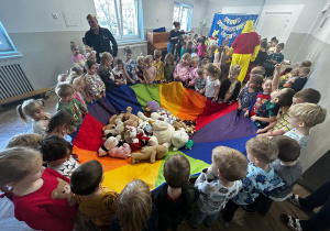 Dzieci trzymają chustę animacyjną, na której leżą pluszowe misie