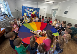 Dzieci trzymają chustę animacyjną, na której leżą pluszowe misie