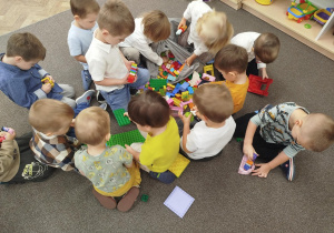 Dzieci na dywanie budują domy z klocków