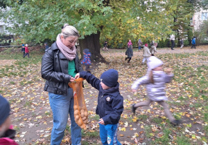 Chłopiec wrzuca do worka swojej grupy znaleziony ziemniak. Worek trzyma nauczycielka grupy II