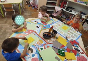 Dzieci przyklejają po kolei elementy papieru tworząc dom