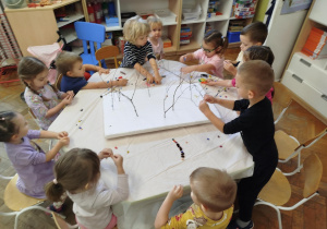 Dzieci ozdabiają gałązki tworząc jesienne drzewka