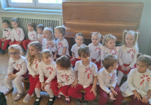 Dzieci siedzą na ławeczkach i słuchają wierszy na temat Polski