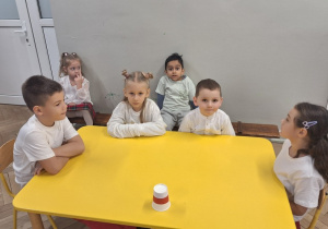 Wybrani reprezentanci grupy siedzą przy stoliku, przy nich na ławeczce siedzą ich koledzy