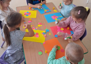 Dzieci przy stoliku wykonyją pracę plastyczną z wykorzystaniem kolorowych kropek