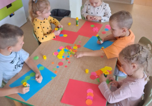 Dzieci przy stoliku wykonyją pracę plastyczną z wykorzystaniem kolorowych kropek