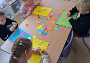 Dzieci przy stoliku wykonyją pracę plastyczną z wykorzystaniem kolorowych kropek