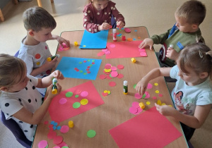 Dzieci przy stoliku wykonyją pracę plastyczną z wykorzystaniem kolorowych kropek