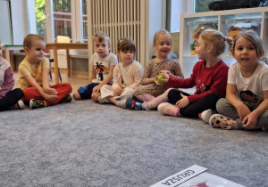 Dzieci siedza w kole i podają sobie jabłko