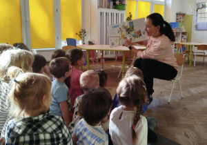 Dzieci siedzą na dywanie i słuchają czytanej książki