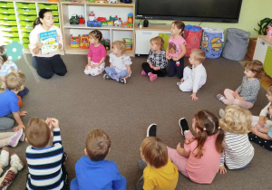 Dzieci siedzą na dywanie i słuchają czytanej książki