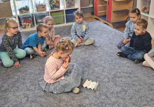 Dziewczynka siedząc w kole prezentuje swoje prawo do rozwijania zaintesresowań, grając na harmonijce