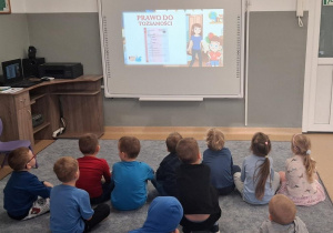 Dzieci na dywanie oglądają prezentację multimedialną o prawach dziecka