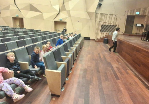 Dzieci siedzą w sali i czekają  na koncert