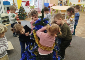 Dzieci ubierają choinkę łańcuchami i kolorowymi bombkami