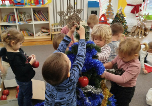 Dzieci dekorują choinkę łańcuchami, chłopczyk zakłada gwiazdę na choinkę