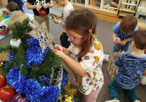 Dziewczynka zawiesza kolorową bombkę na choinkę