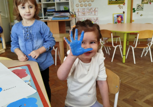 Dziewczynka odciska na kartonie swoją dłoń pomalowaną na niebiesko