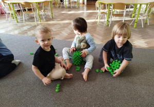 Chłopcy siedzą na dywanie z klockami w kolorze zielonym