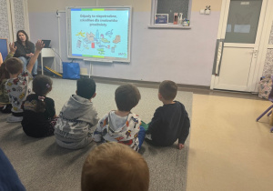 Dzieci siedzą przed tablica multimedialną i omawiają z prowadzącą oglądaną prezentację
